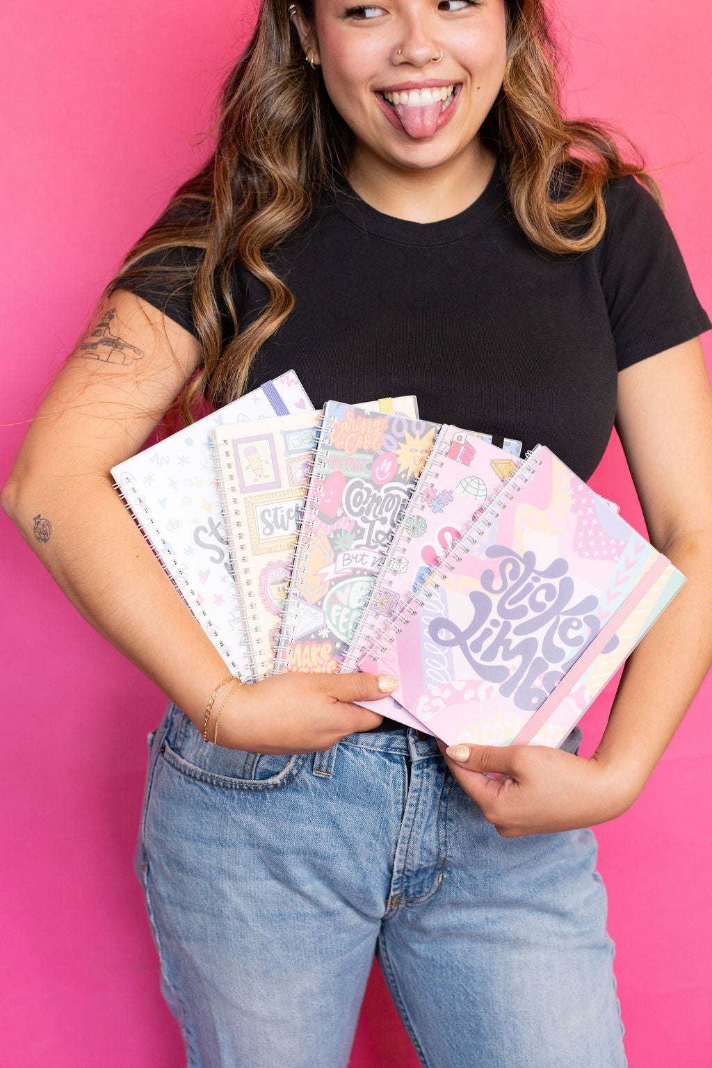 Person holding colorful notebooks against a pink background