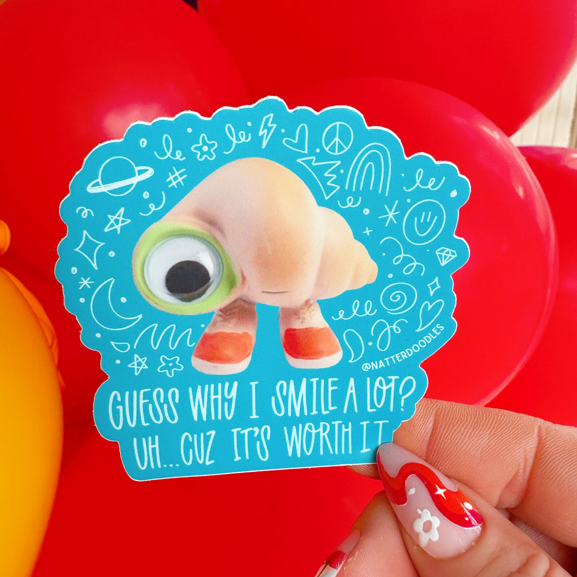 Sticker with a cartoon character and text held in front of red balloons