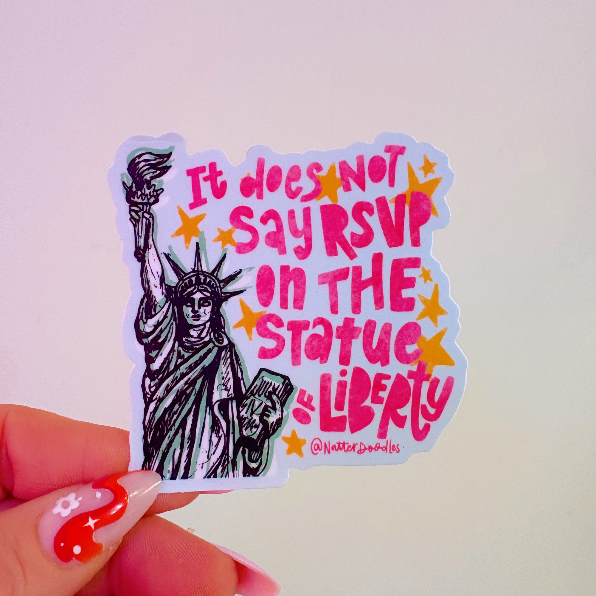 Sticker with Statue of Liberty graphic and text held by a hand with red nail polish.