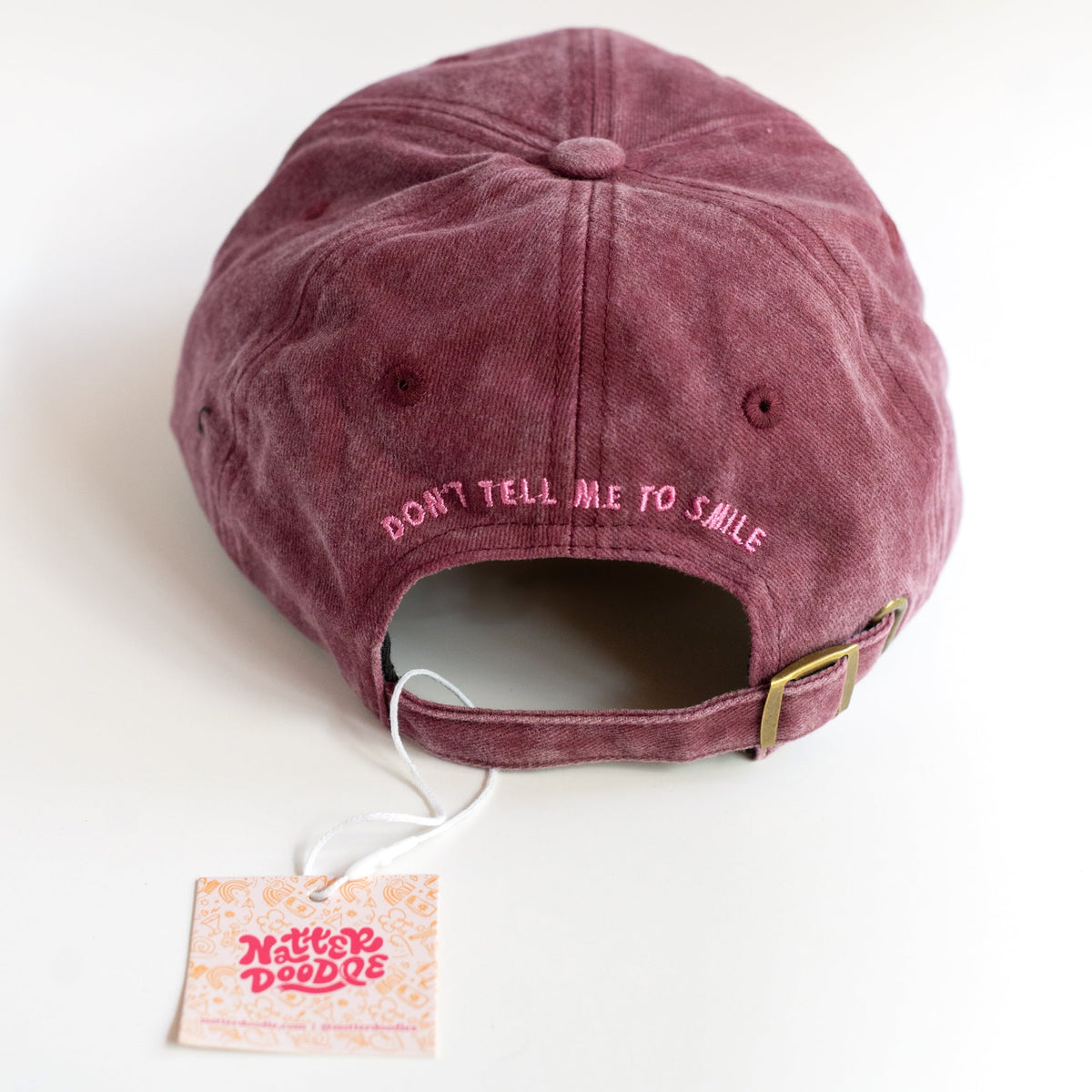 Back of the dad cap with Don't Tell Me to Smile embroidery and gold-tone metal clasp