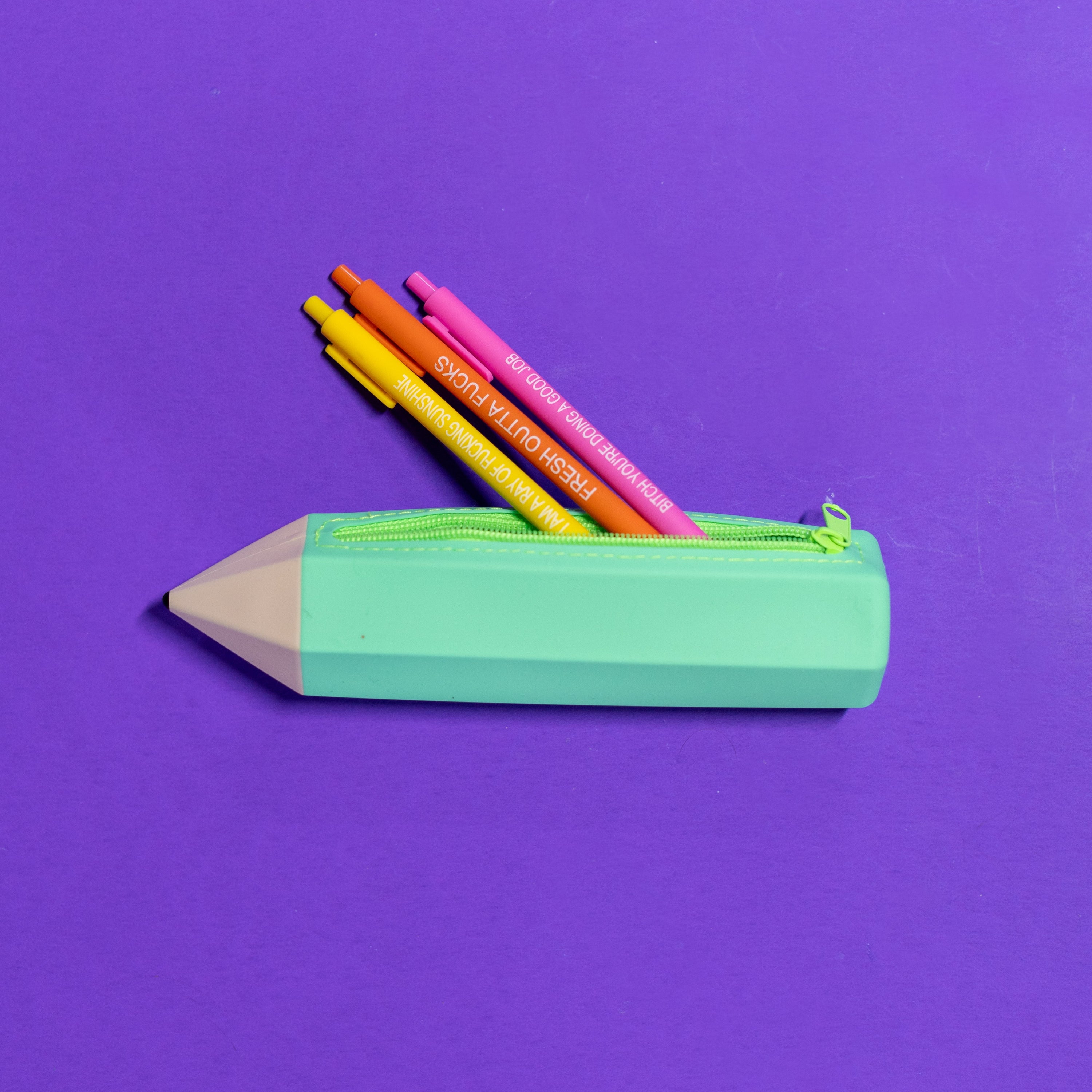 Green pencil-shaped zipper pouch with colorful pencils on a purple background