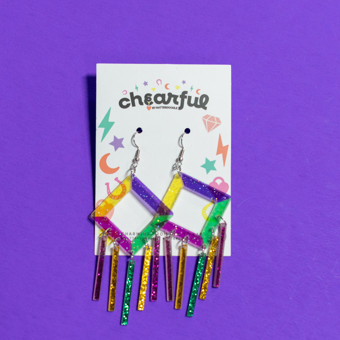 Colorful earrings on a 'chearful' branded card against a purple background