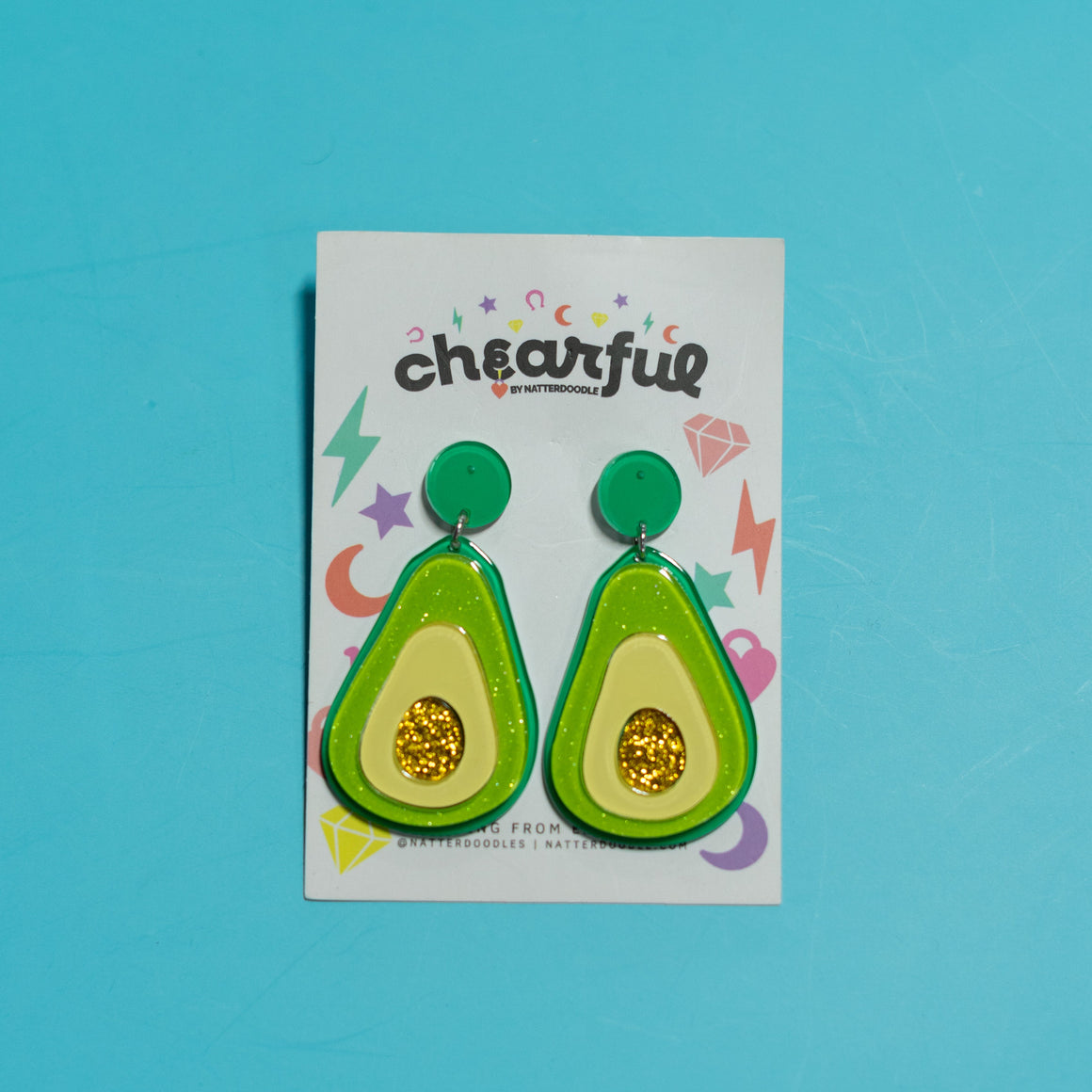 Avocado-shaped earrings on a 'cheerful' branded card against a blue background