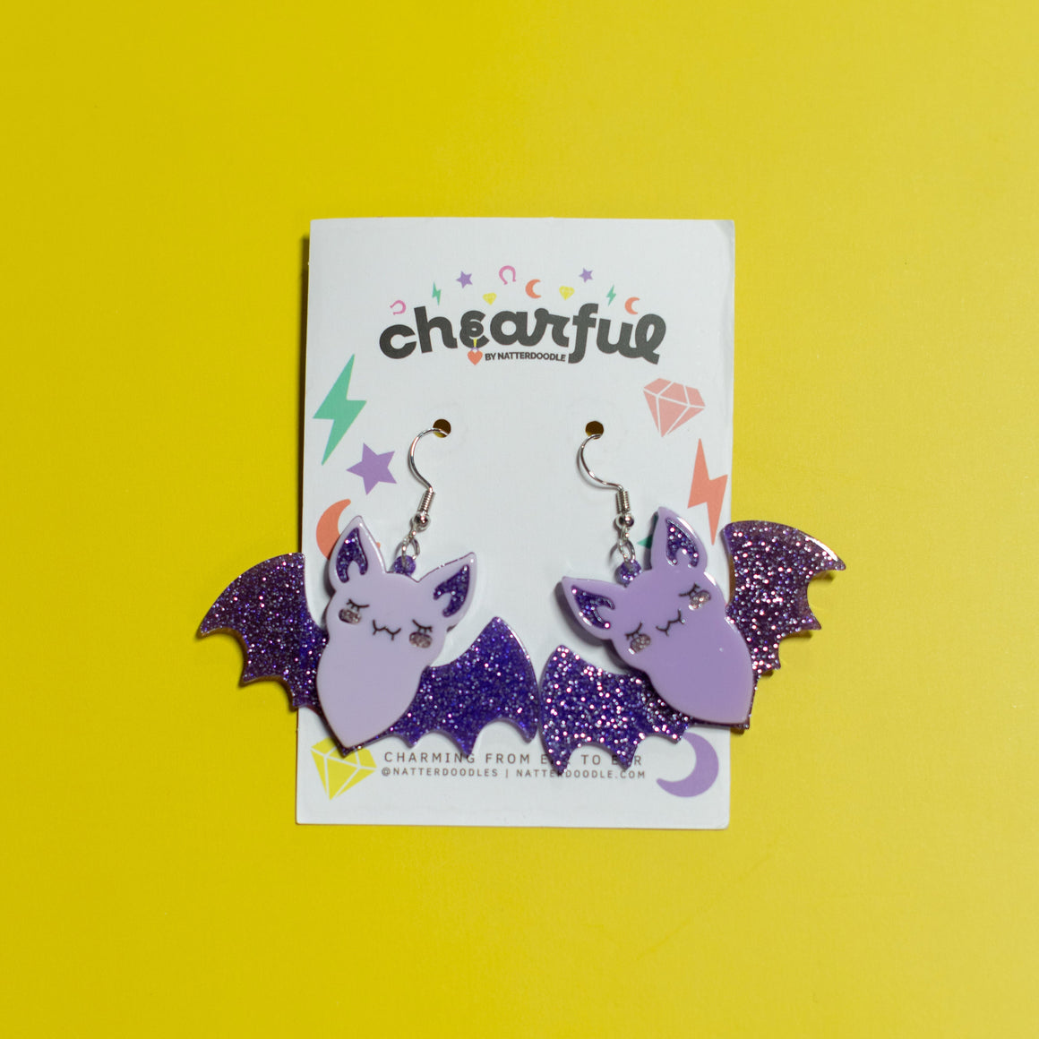 Bat-shaped earrings on a 'cheerful' branded card against a yellow background