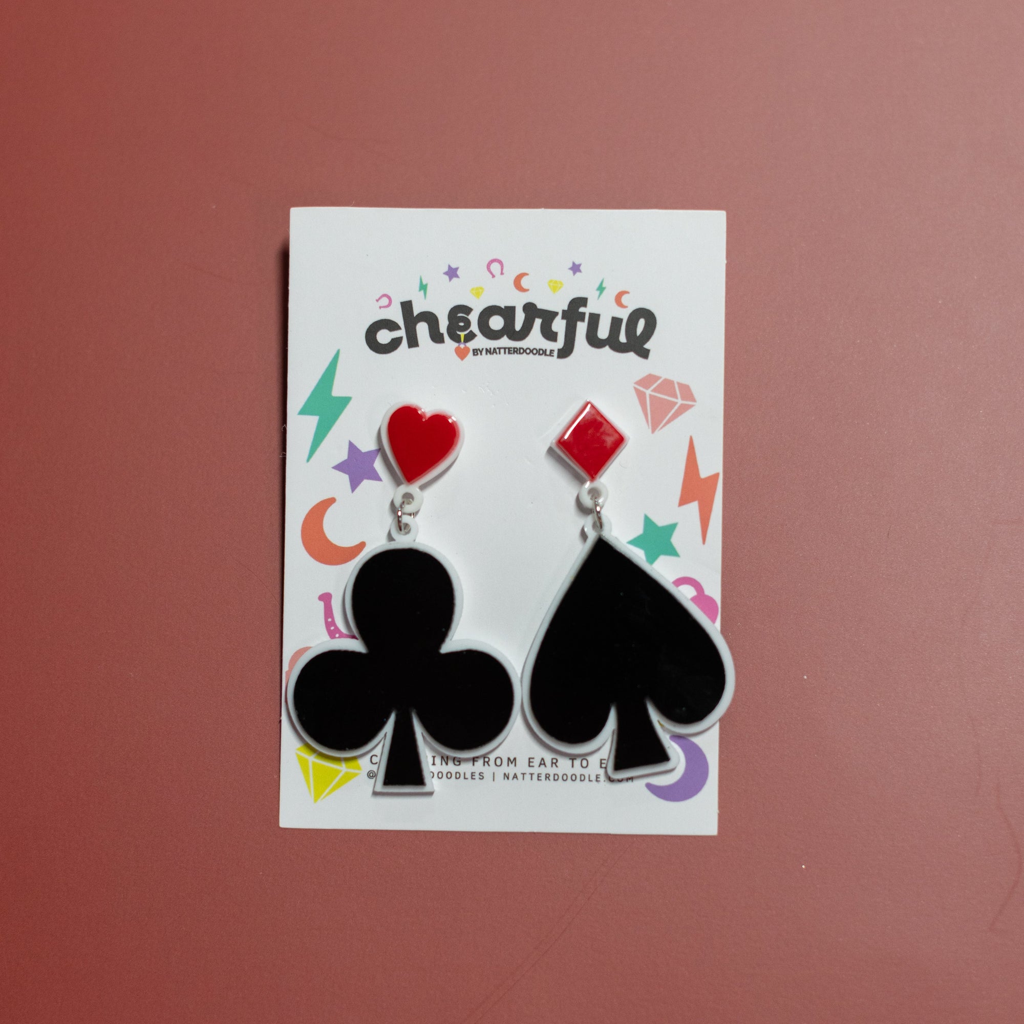 Pair of earrings with club and spade symbols on a 'cheerful' branded card against a red background
