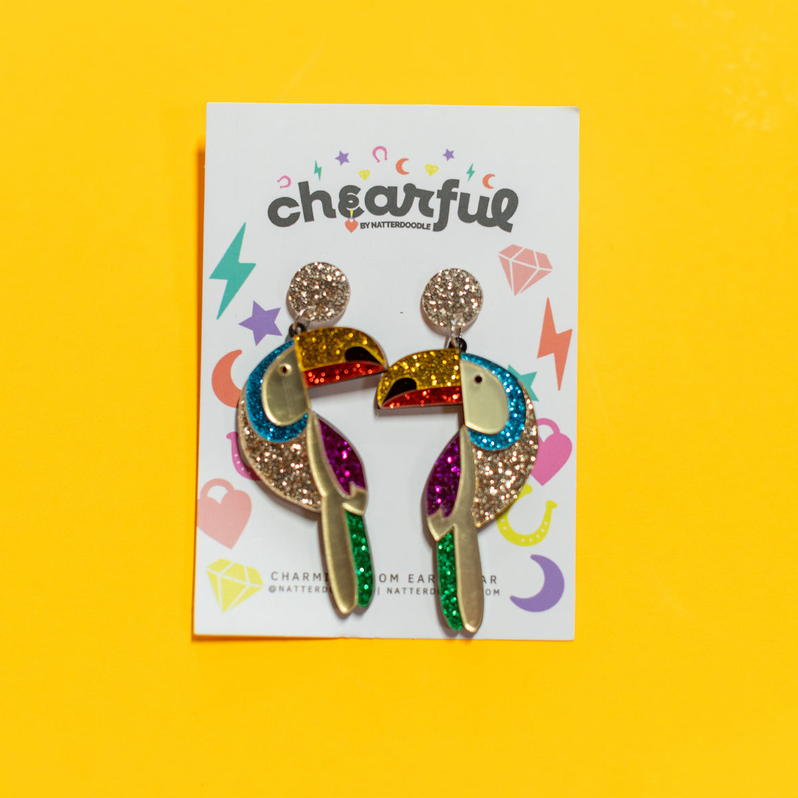 Colorful earrings on a 'cheerful' branded card against a yellow background