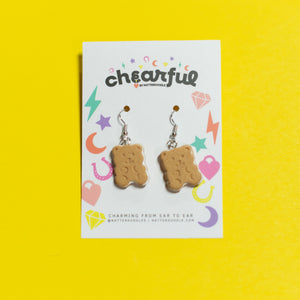 Graham cracker-shaped earrings on a 'cheerful' branded card against a yellow background