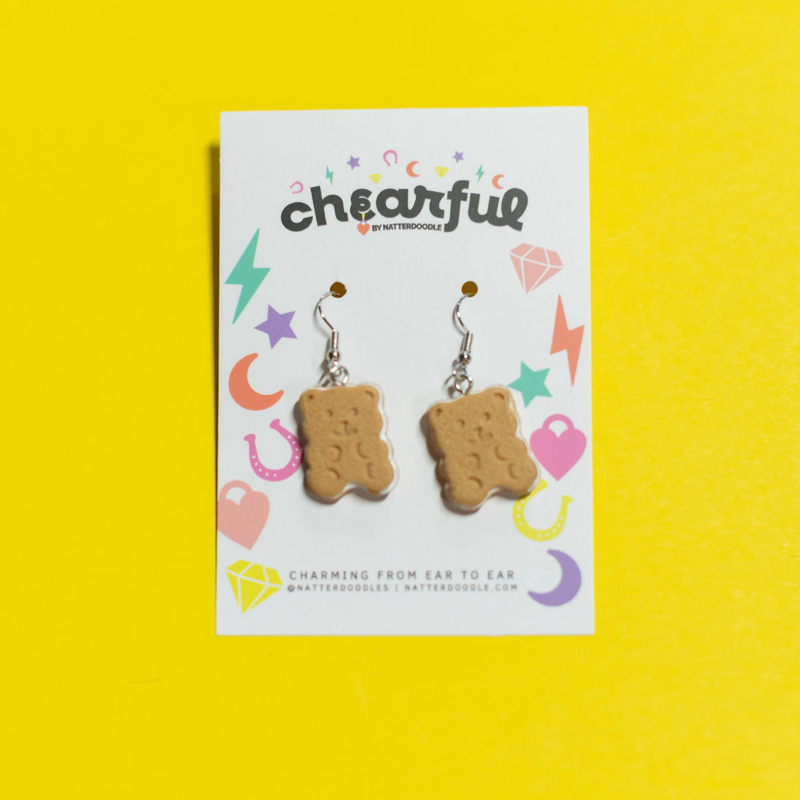 Graham cracker-shaped earrings on a 'cheerful' branded card against a yellow background