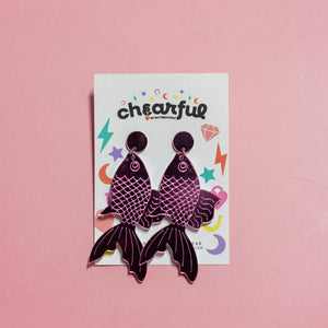 Pair of purple fish-shaped earrings on a 'chearful' branded card against a pink background
