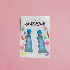 Pair of blue earrings with blue paint cans on a 'cheerful' branded card against a pink background