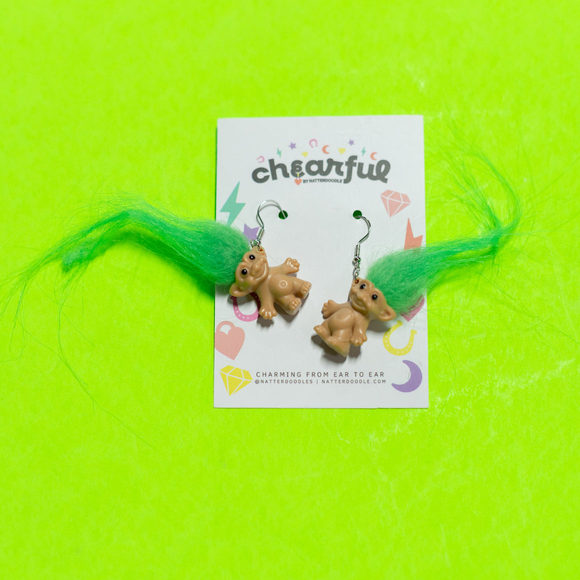 Pair of bear-shaped earrings on a 'cheerful' branded card against a bright green background