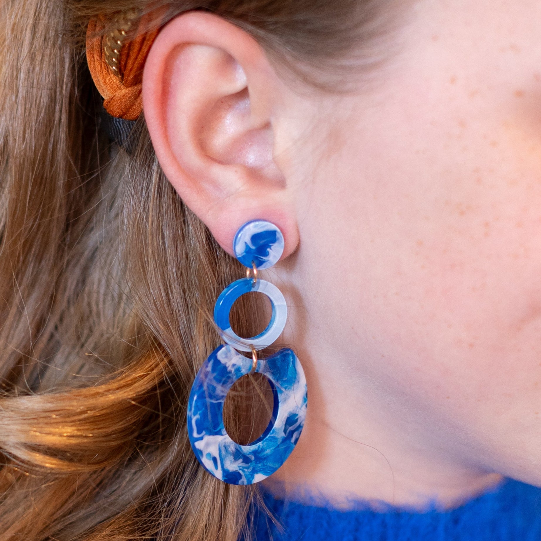 Close-up of a person wearing blue earrings with an orange headband against an orange background