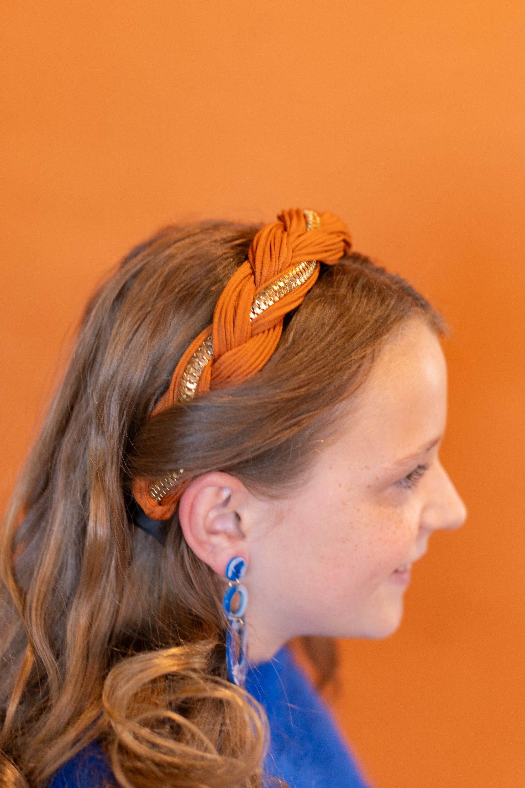 Girl wearing an orange headband with braided design against an orange background
