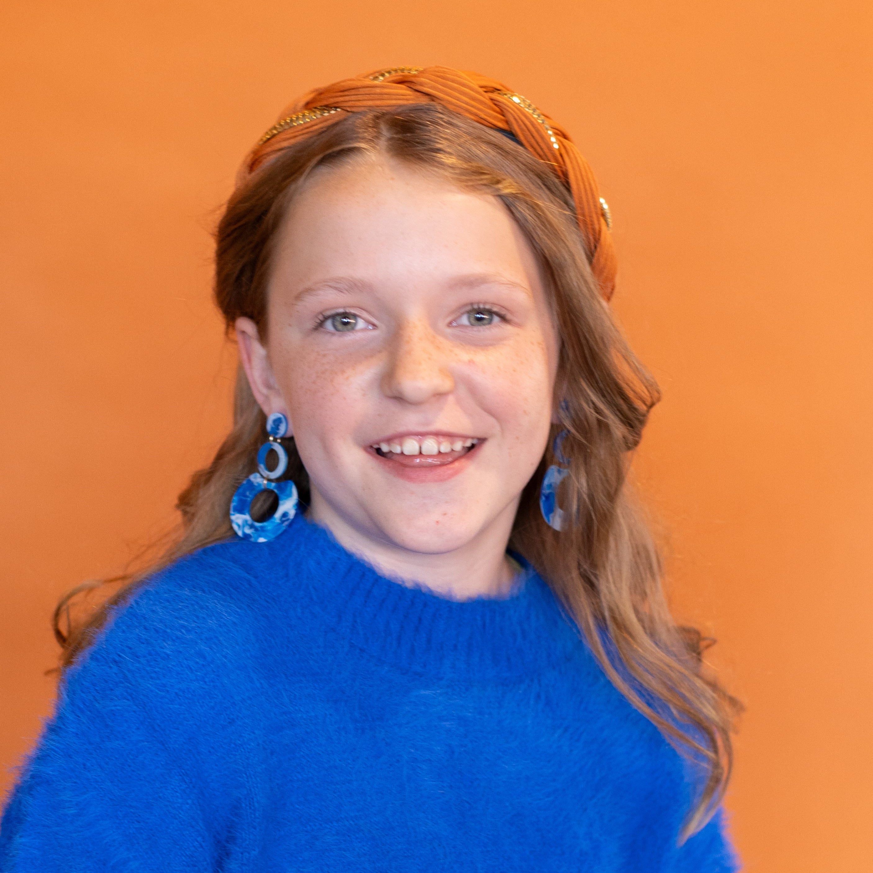 Young girl wearing a blue sweater and white dress against an orange background