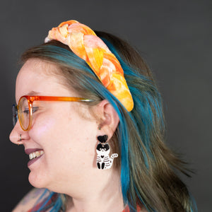 Person with blue hair, colorful headband, and earrings against a dark background