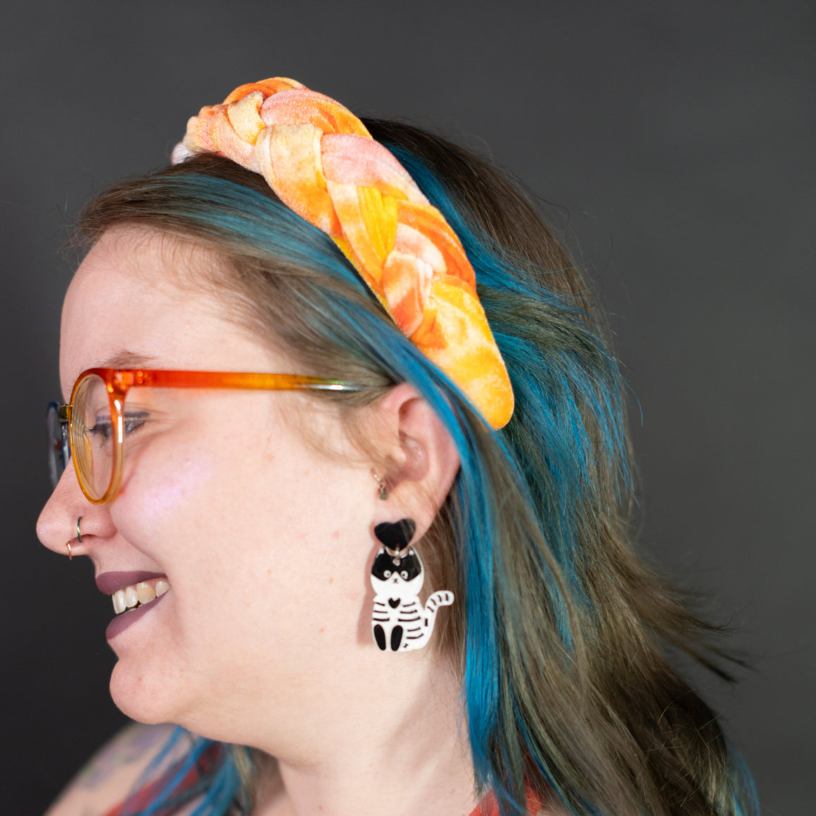Person with blue hair, colorful headband, and earrings against a dark background