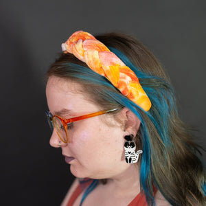 Person with colorful braided headband and tattoos wearing glasses against a dark background