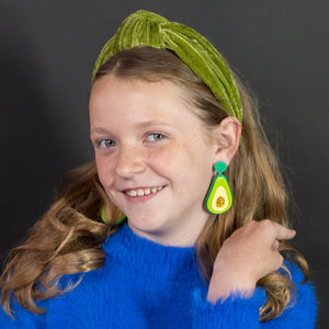 Young girl wearing a blue sweater and green headband against a black background