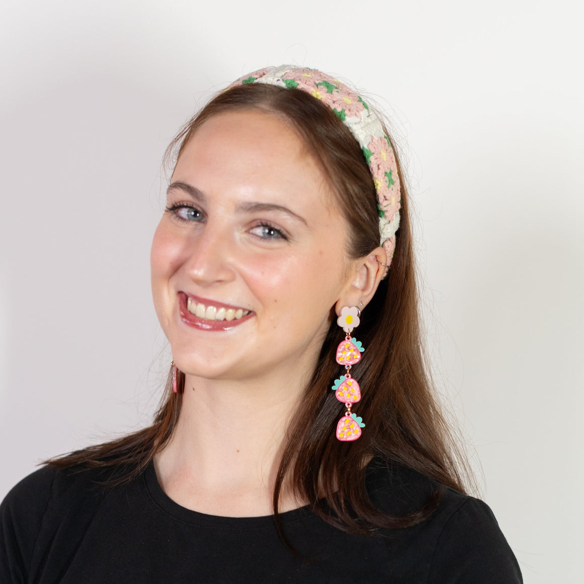 Woman wearing a black top and floral headband with earrings on a white background