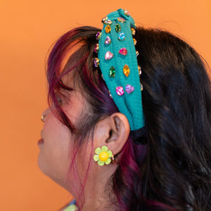 Person wearing a colorful headband with gemstones and a floral earring against an orange background