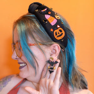 Person with colorful hair and accessories, including a headband and earrings, against an orange background.