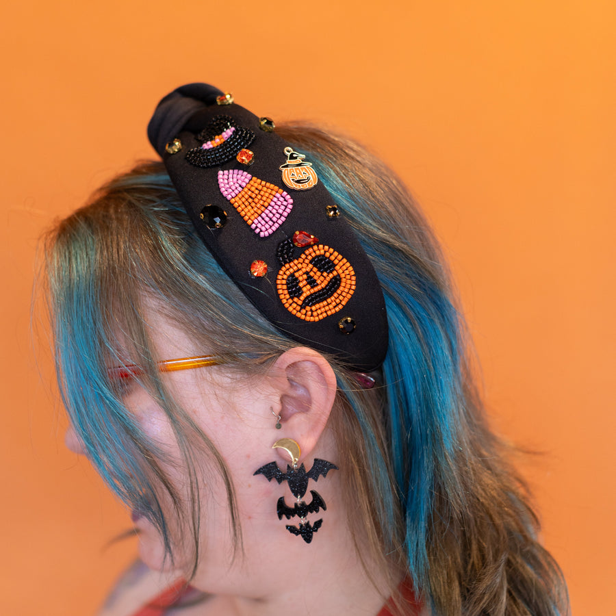 Person with colorful hair and accessories, including a headband and earrings, against an orange background.