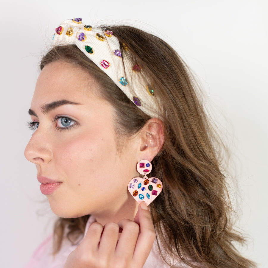 Person wearing a colorful headband with gemstones and a floral earring against an orange background