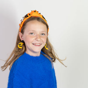 Young girl wearing an orange Halloween headband with black spiders on a white background