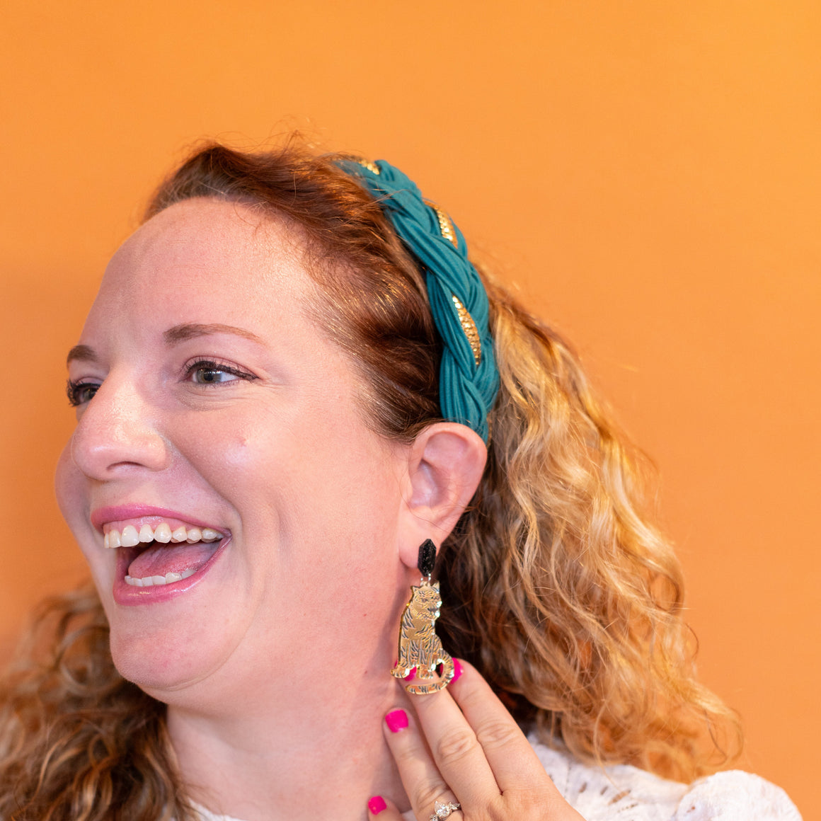 Woman wearing a teal headband and white lace top, holding an earring.