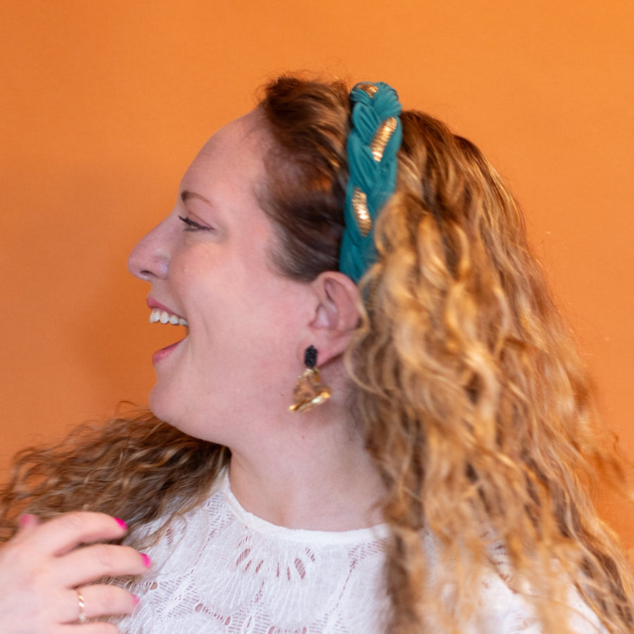 Woman wearing a teal headband and white lace top, holding an earring.