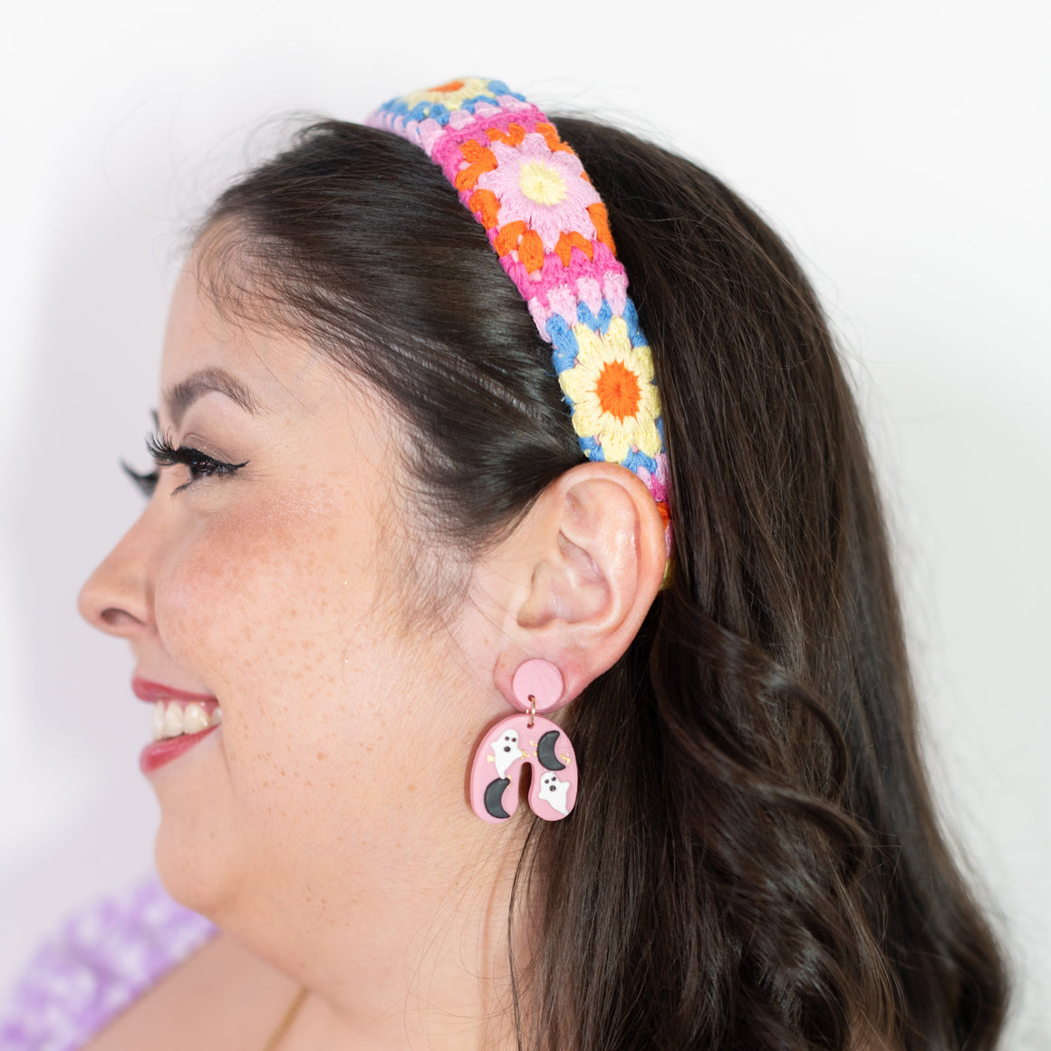 Woman wearing a colorful floral headband and pink earrings with a white background