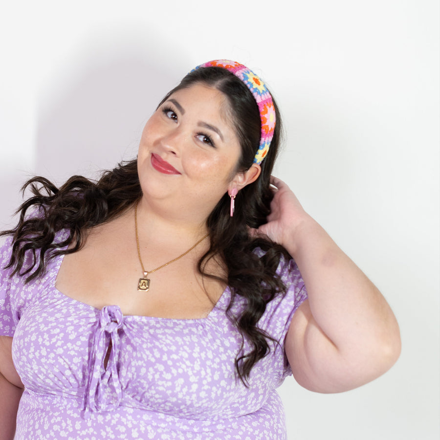 Woman wearing a colorful floral headband and pink earrings with a white background