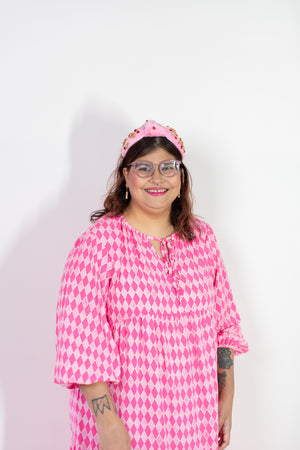 Person wearing a pink and white patterned dress with a headband on a white background