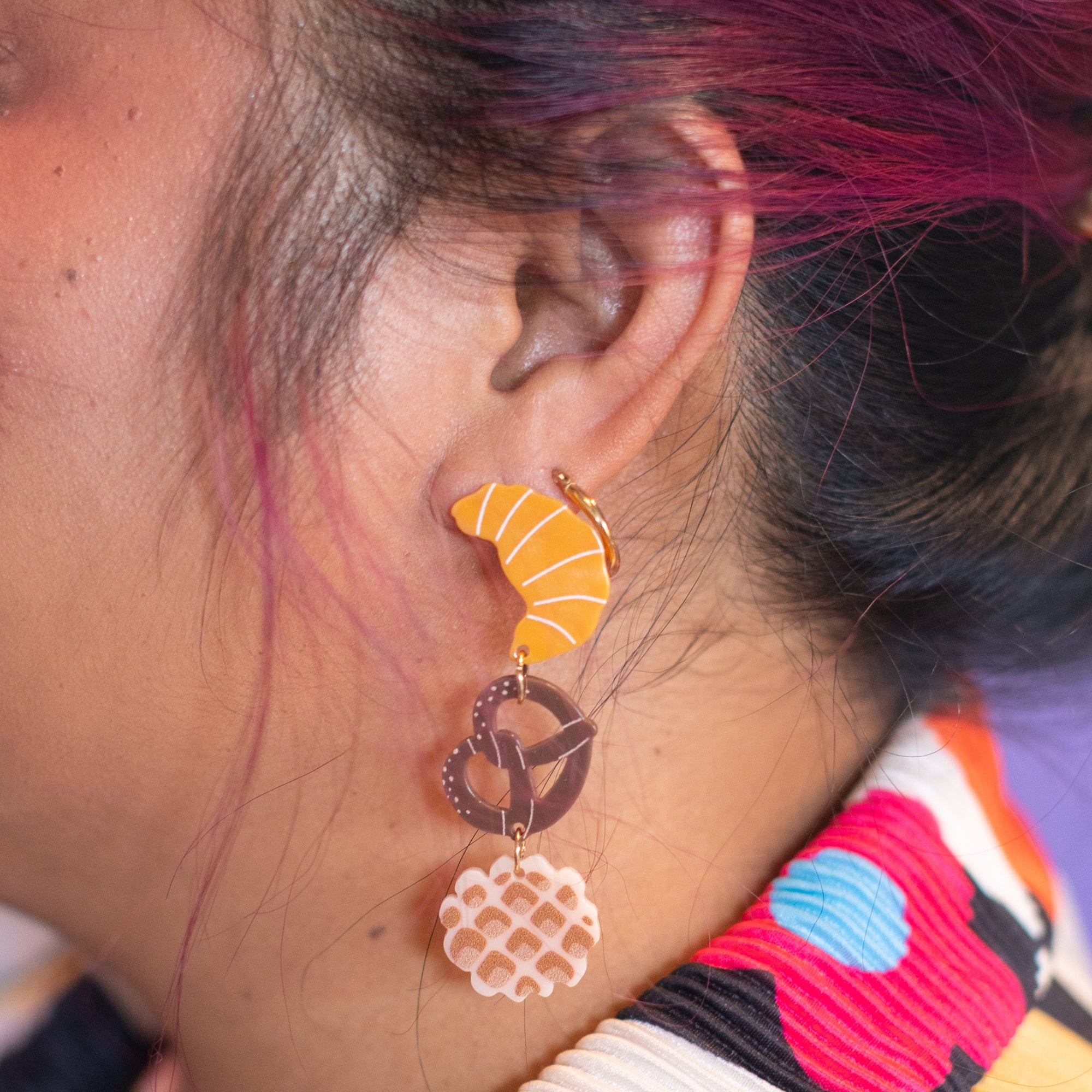 Close-up of a person wearing colorful earrings with a vibrant background