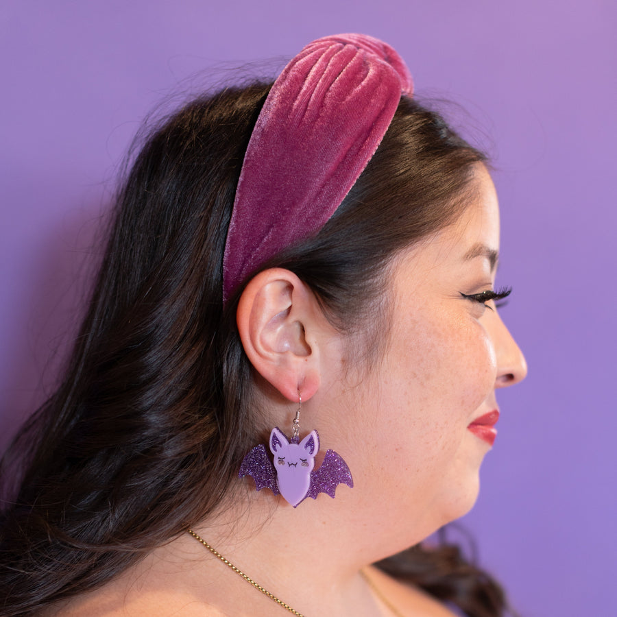 Bat-shaped earrings on a 'cheerful' branded card against a yellow background
