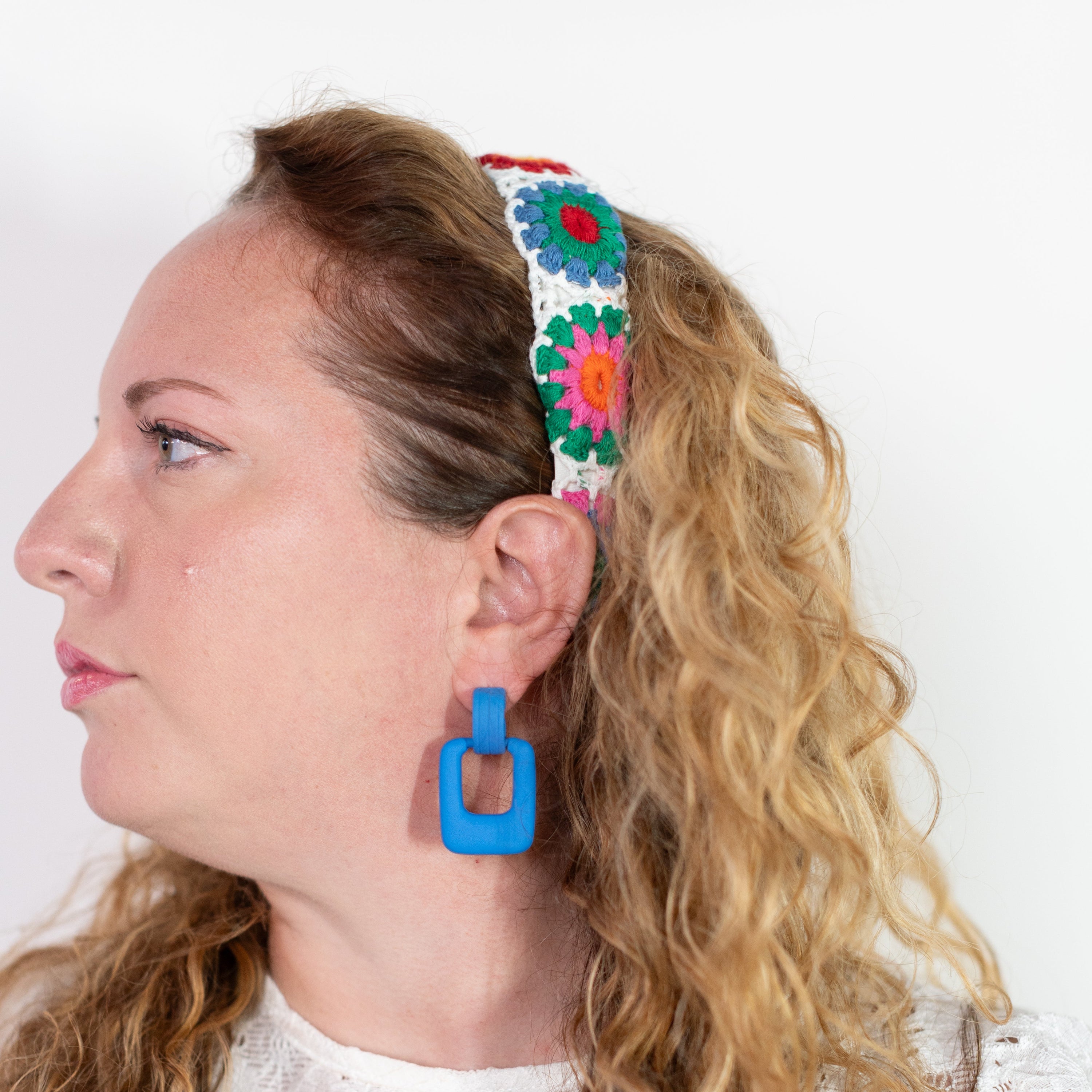 Woman wearing a colorful headband and blue earrings against a white background