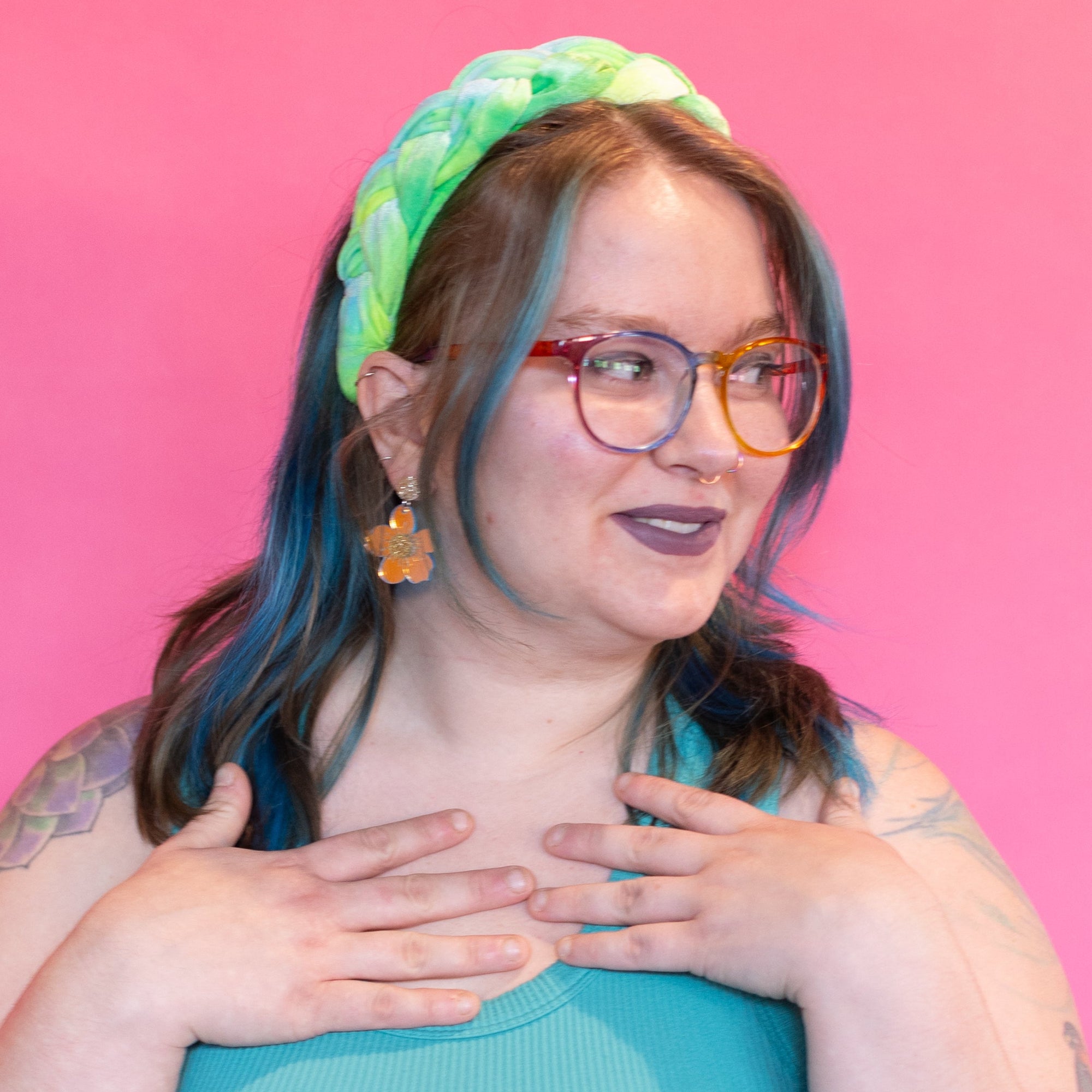 Person wearing a teal top and denim shorts with a colorful headband against a pink background