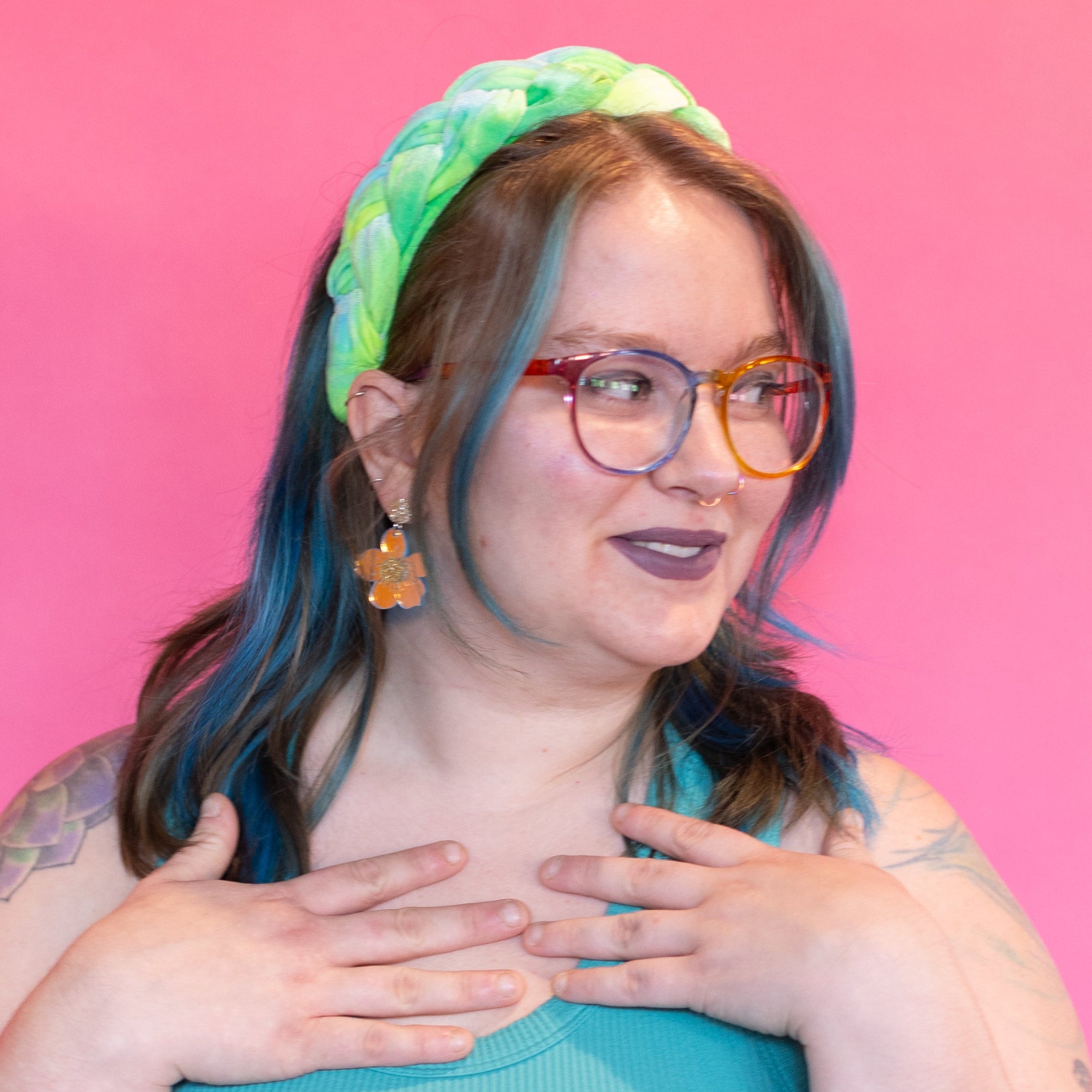 Person wearing a teal top and denim shorts with a colorful headband against a pink background