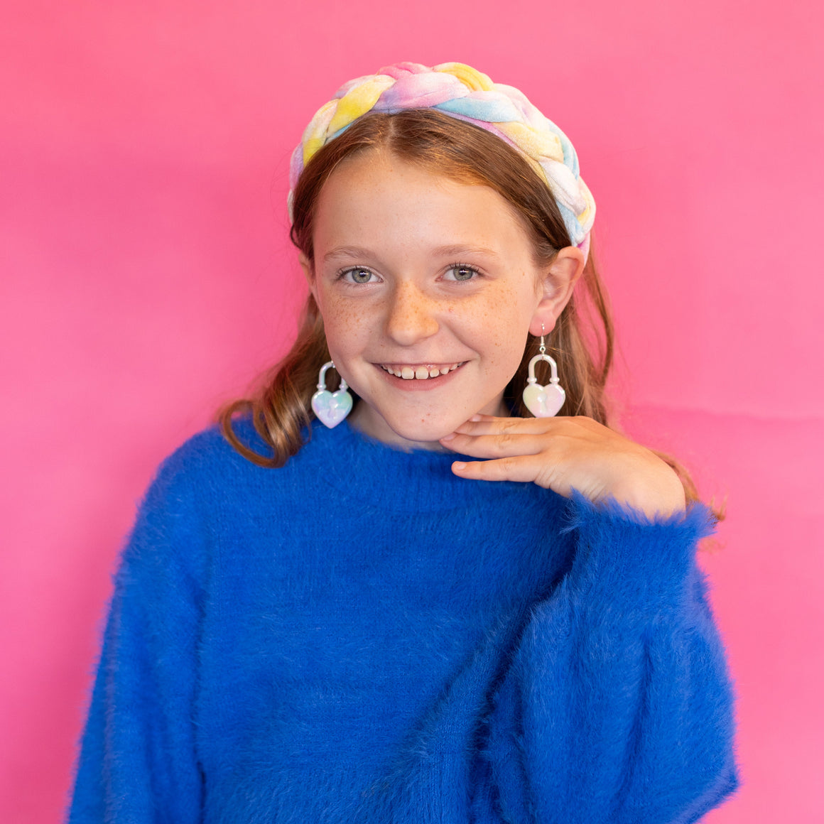 Young girl wearing a blue sweater and white skirt against a pink background