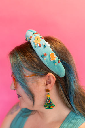 Person wearing a turquoise headband with colorful decorations against a pink background