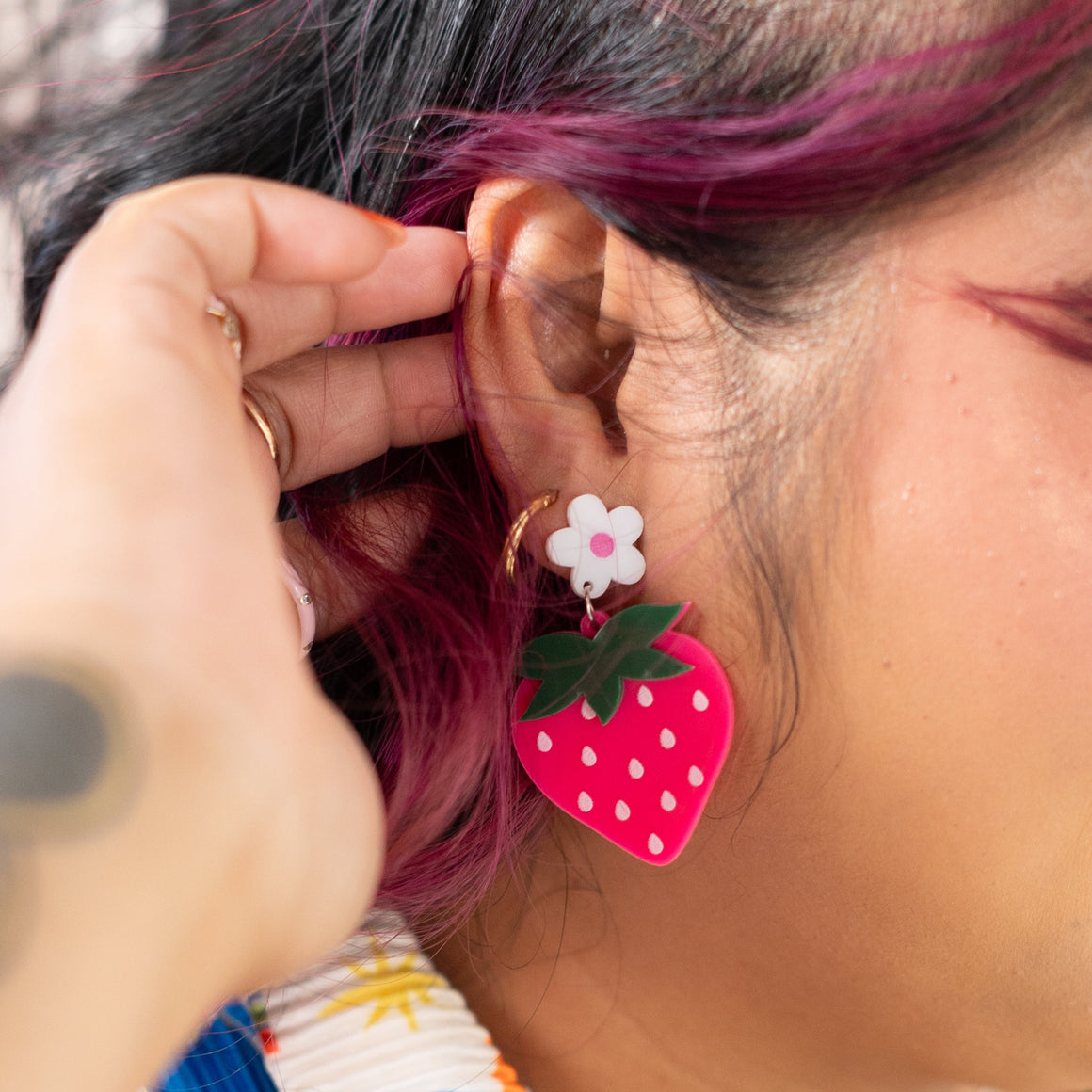 Person wearing colorful earrings with strawberry design, close-up of face and earrings.