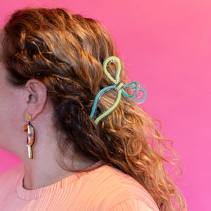 Person with a colorful hair tie in their hair against a pink background