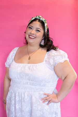 Woman wearing a white dress and floral headband against a pink background