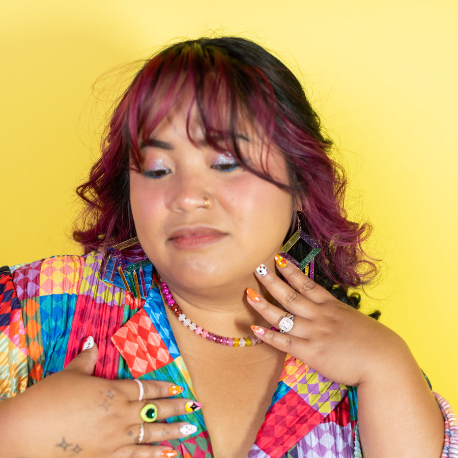 Colorful earrings on a 'chearful' branded card against a purple background