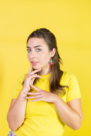 Woman in a yellow shirt posing with a thoughtful expression on a yellow background