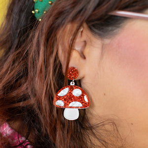 Close-up of a person wearing red and white mushroom-shaped earrings with a green headband against a yellow background.