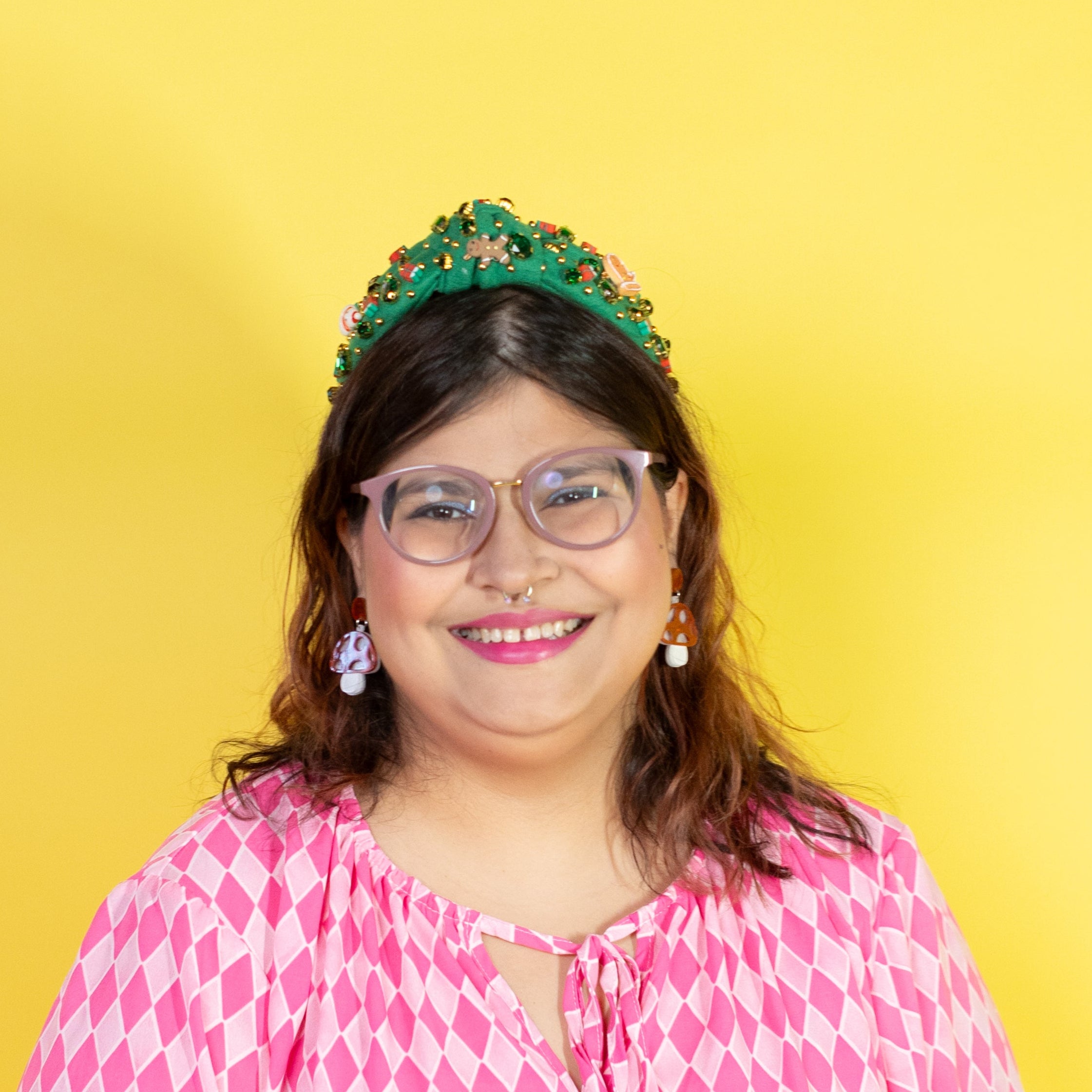 Person wearing a pink patterned dress and green headband against a yellow background
