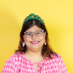 Person wearing a pink patterned dress and green headband against a yellow background