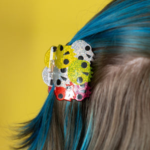 Person with colorful hair clips in blue and gray hair against a yellow background