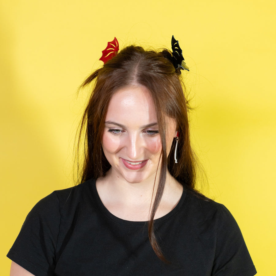 Person with long hair wearing black and red hair clips against a yellow background